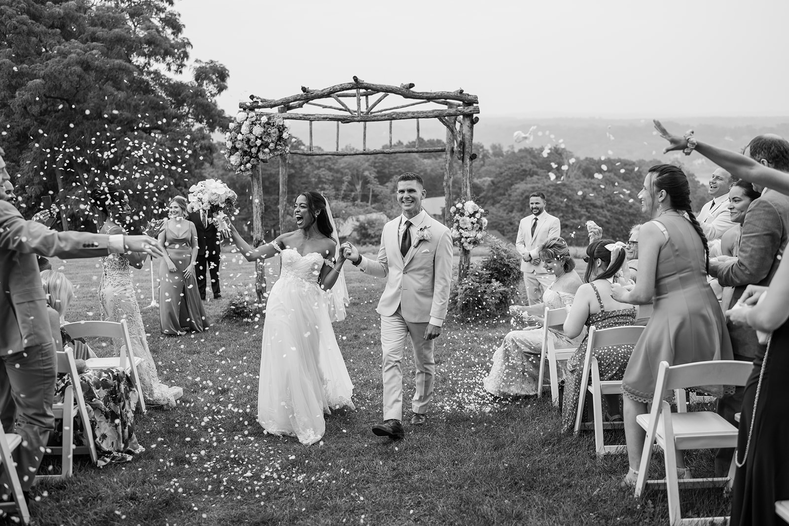 Bride and groom walking back down the aisle through falling petals after their hilltop ceremony at Red Maple Vineyard, black and white