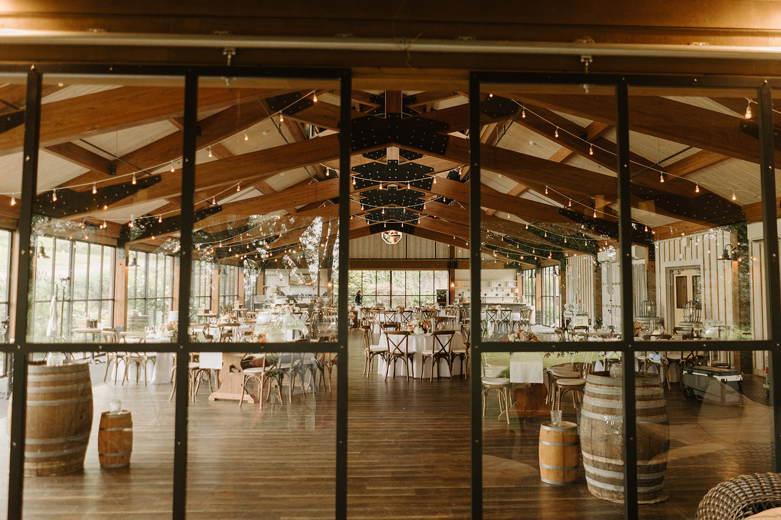 Reception space set beneath string lights inside the timber barn with wine barrels.