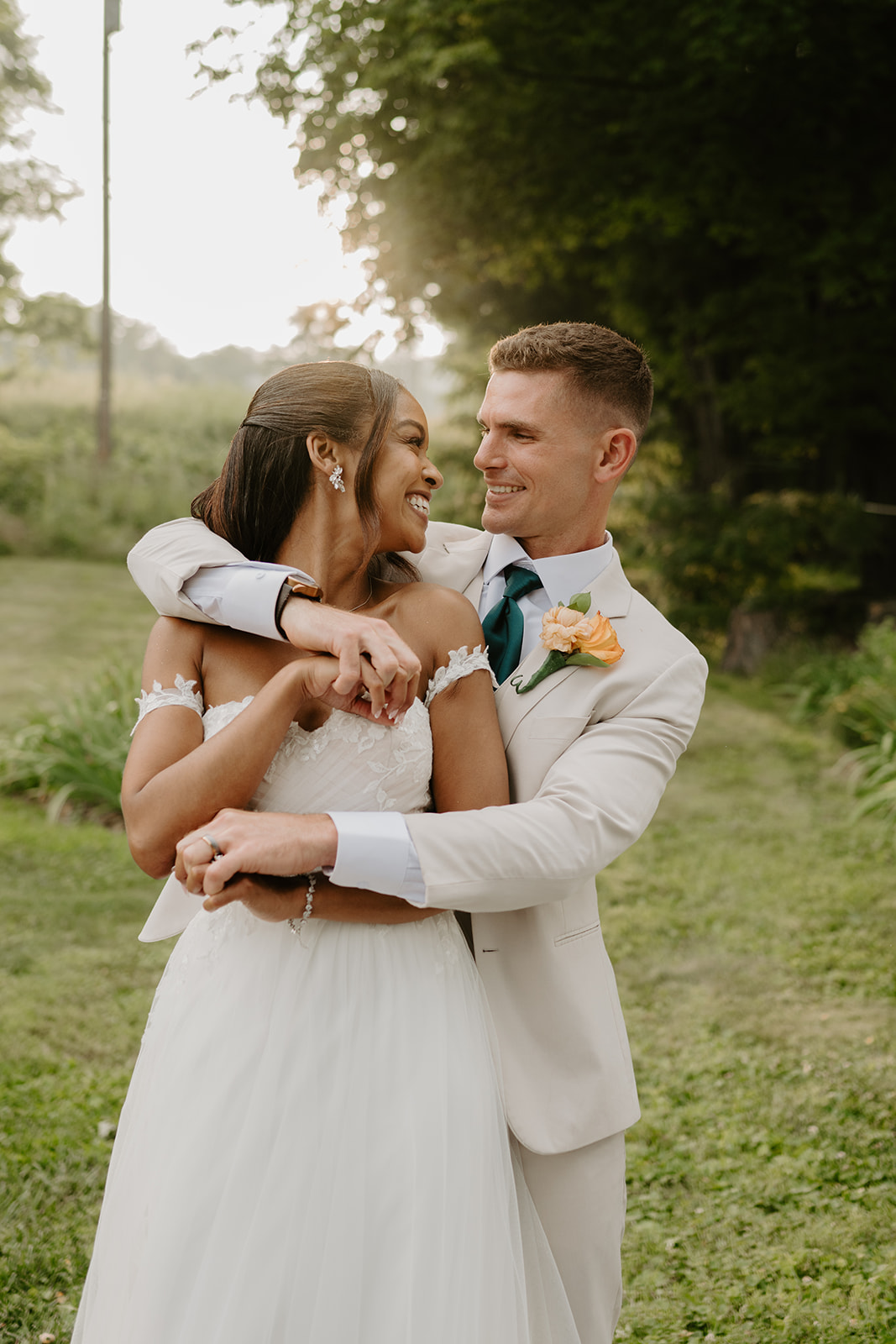Bride and groom hold each other close as golden evening light filters through the trees.