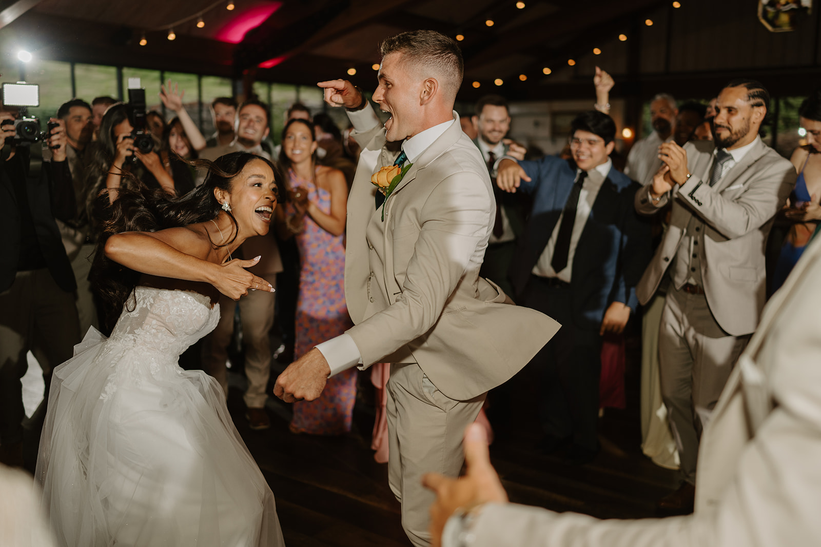 Bride and groom dance surrounded by cheering guests on the packed dance floor.