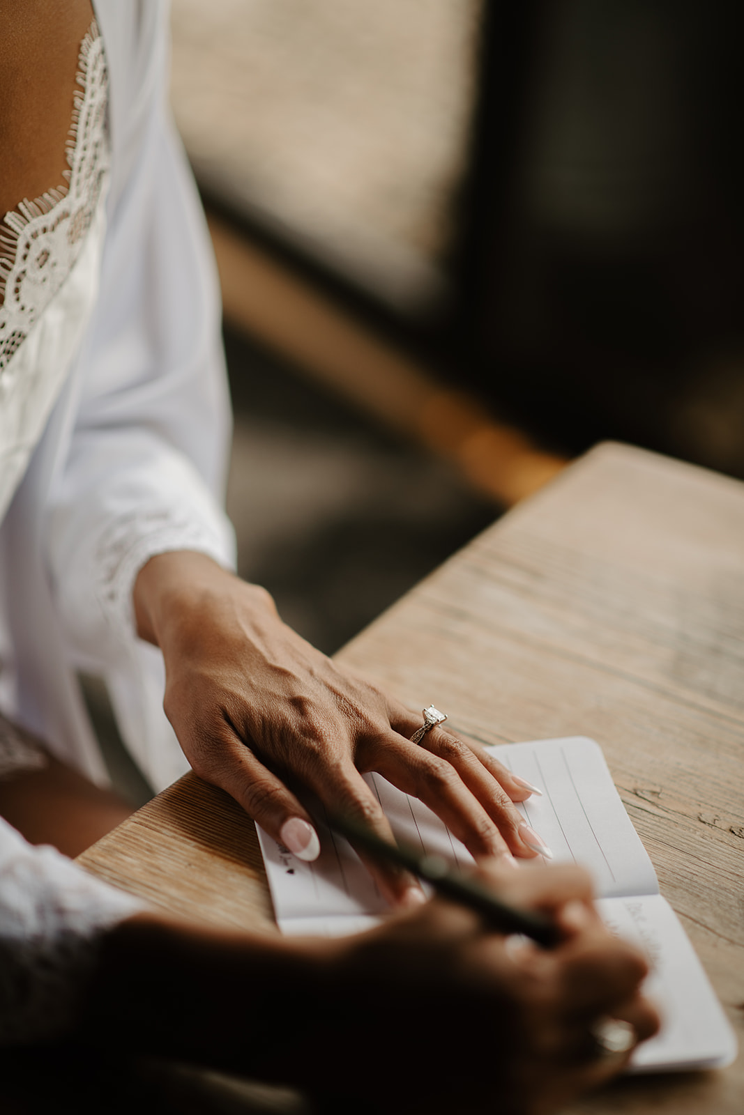 The bride's hands rest on a wooden table as she writes in her vow book.