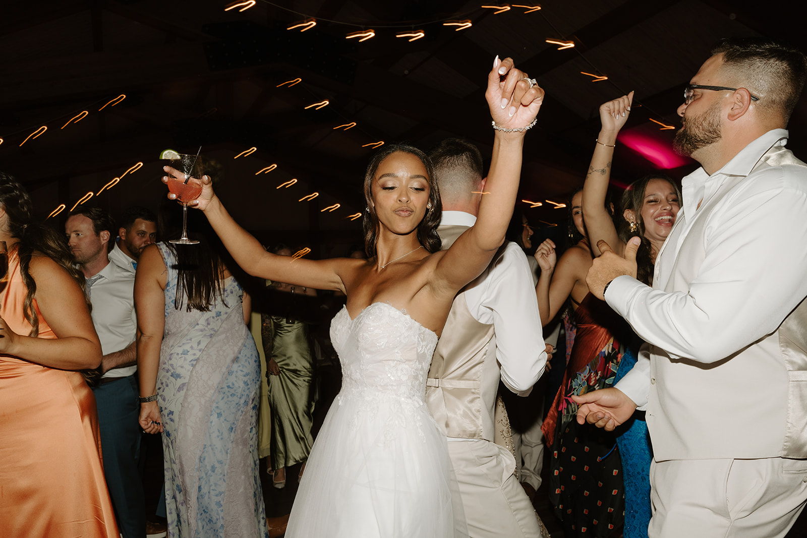 Bride dances with a drink in hand as the party fills the barn floor.