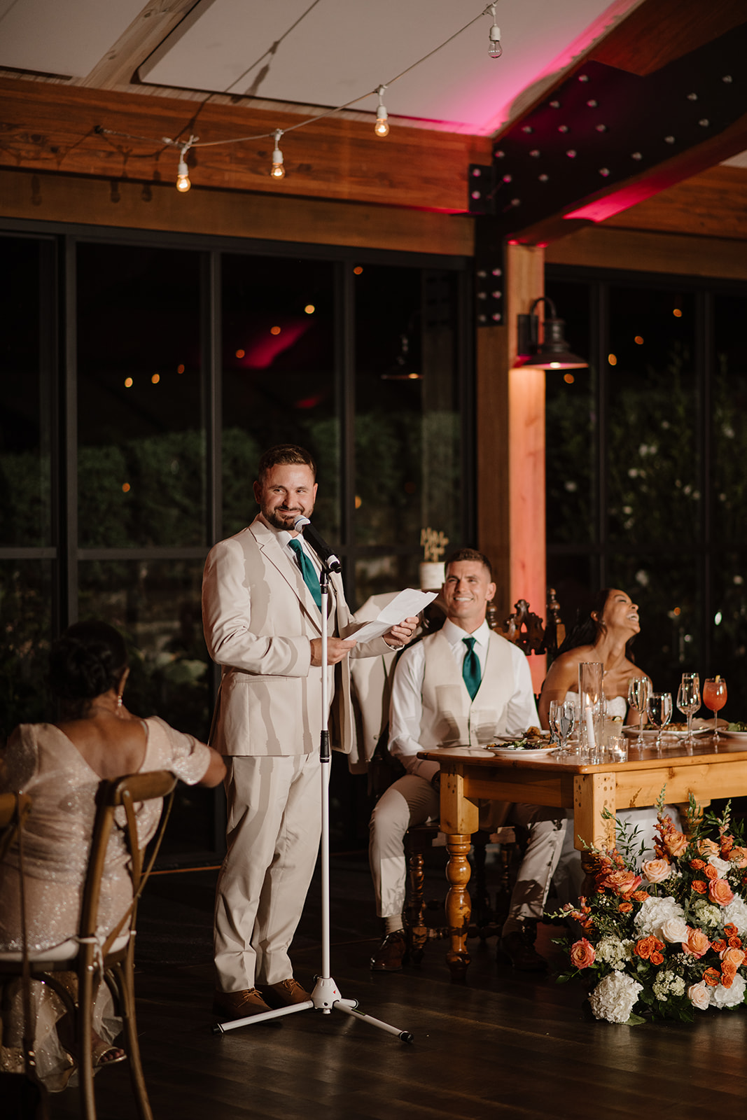 Best man delivers a toast beside the newlyweds at their flower-lined sweetheart table.