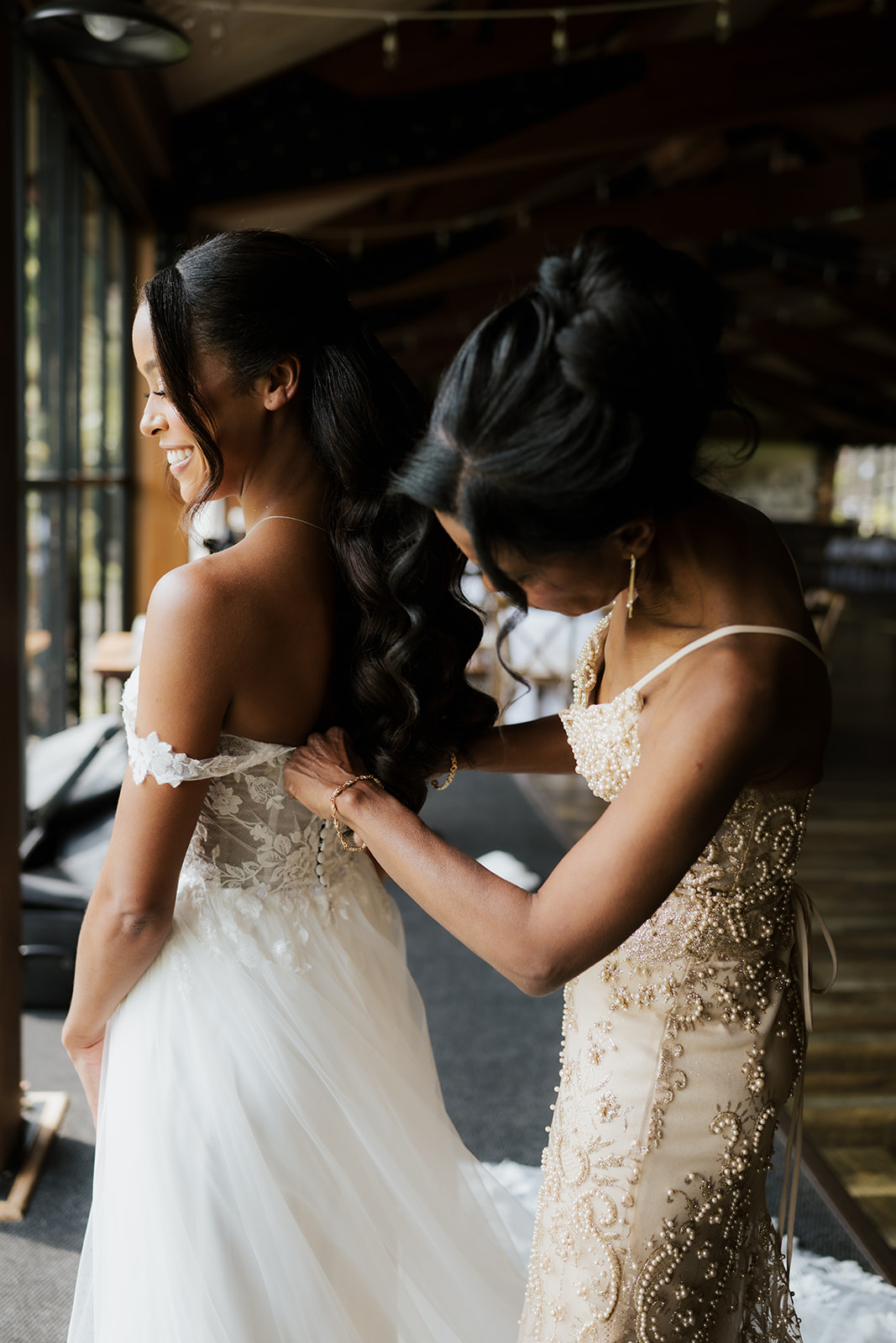 Bridesmaid helps fasten the back of the bride's lace gown.