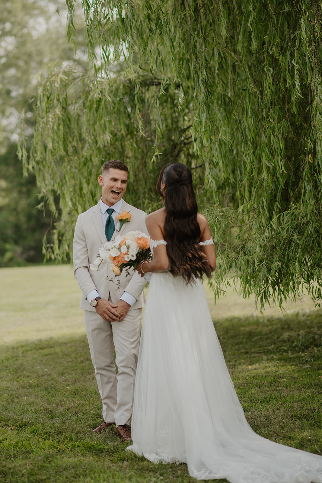Bride and groom stand together beneath the willow, her lace train across the grass.