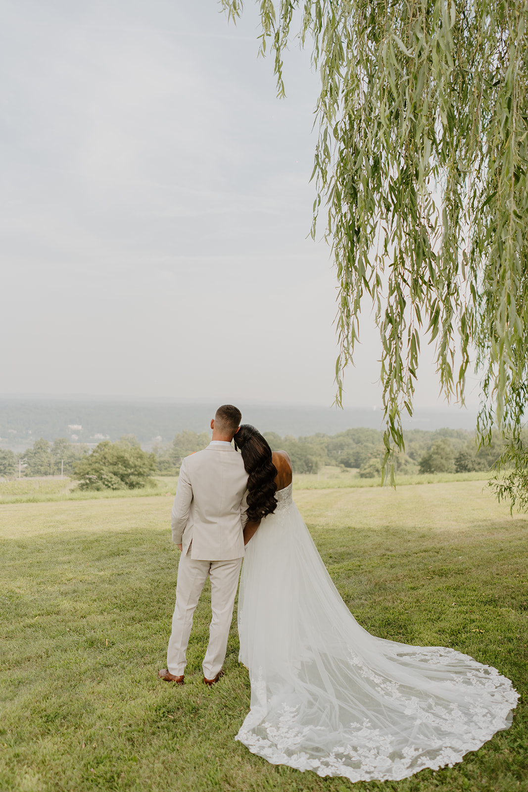 Bride and groom walk away toward the open field, her lace train trailing behind.