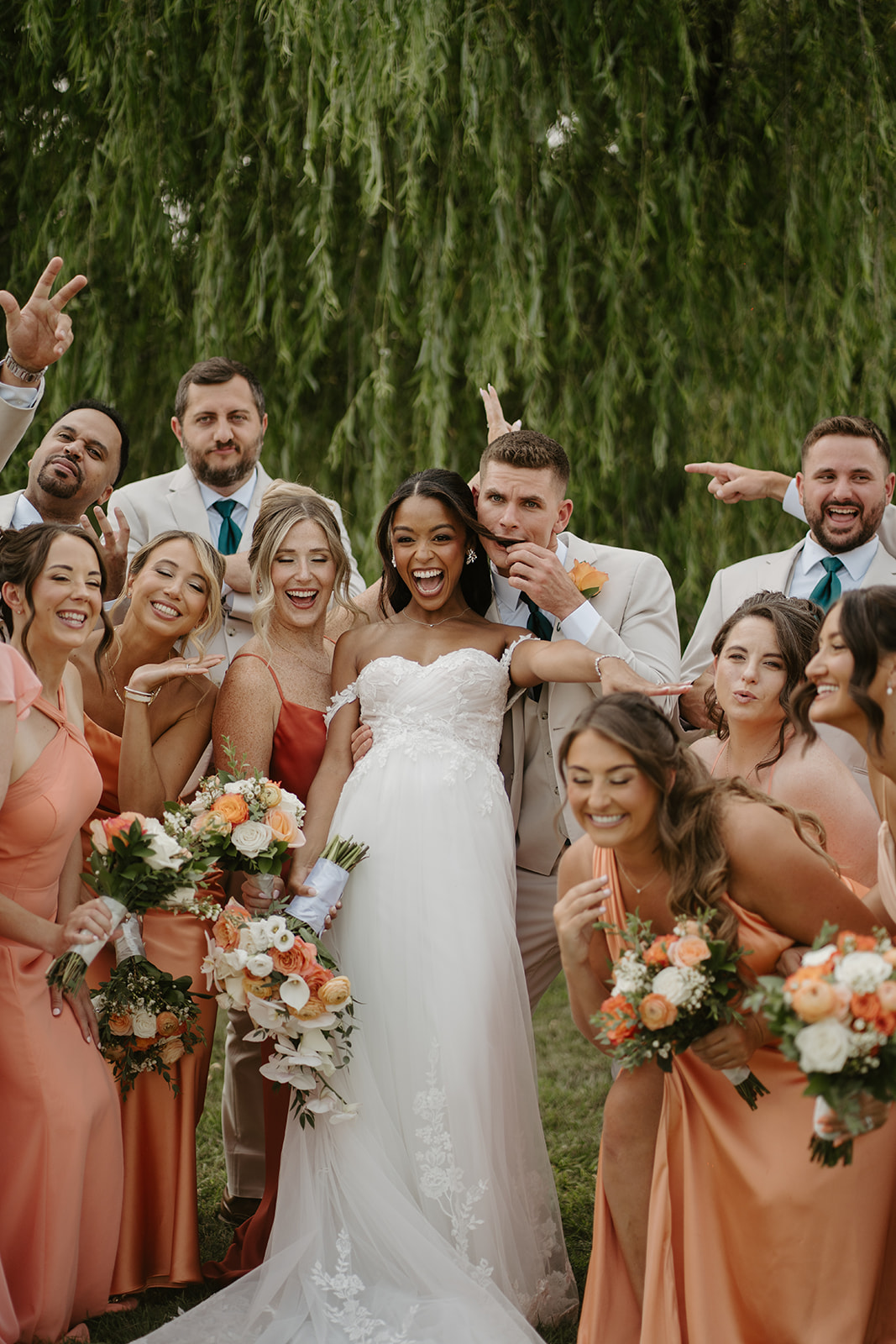 Bride laughs at the centre of her bridal party in coral and peach gowns.