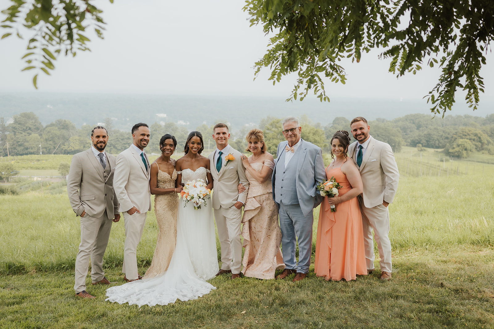 Bride and groom pose with family and bridal party beneath the trees.