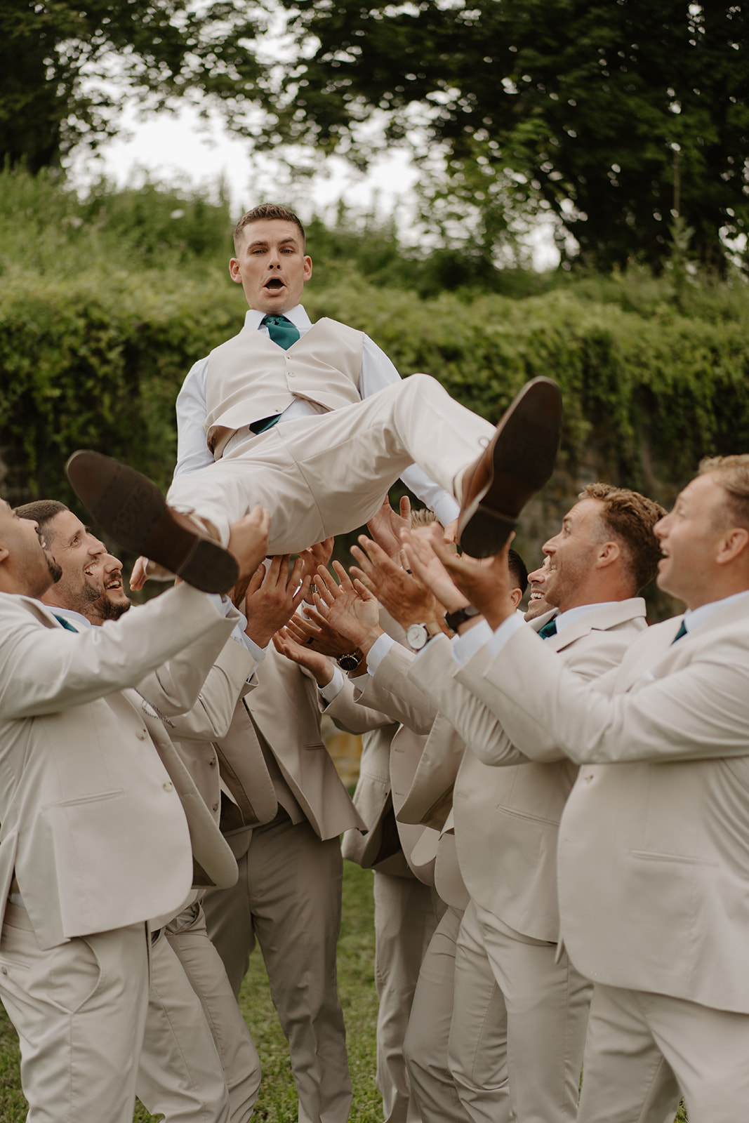 Groomsmen toss the groom high into the air, catching him with cheers.