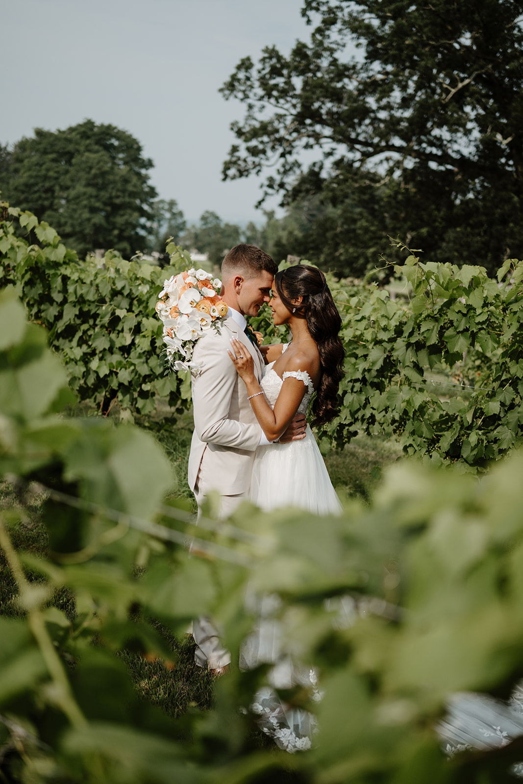 Bride and groom lean in for a kiss, framed by grapevines and leaves.