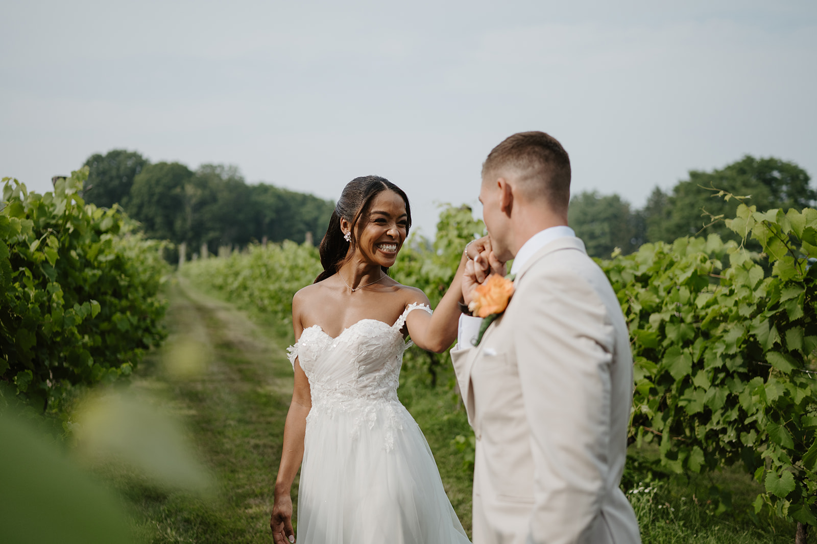Bride laughs as the groom leans in close between the vineyard rows.