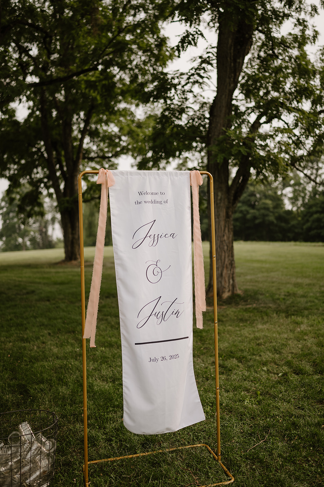 Calligraphed welcome sign hangs from a gold stand on the lawn beneath the trees.