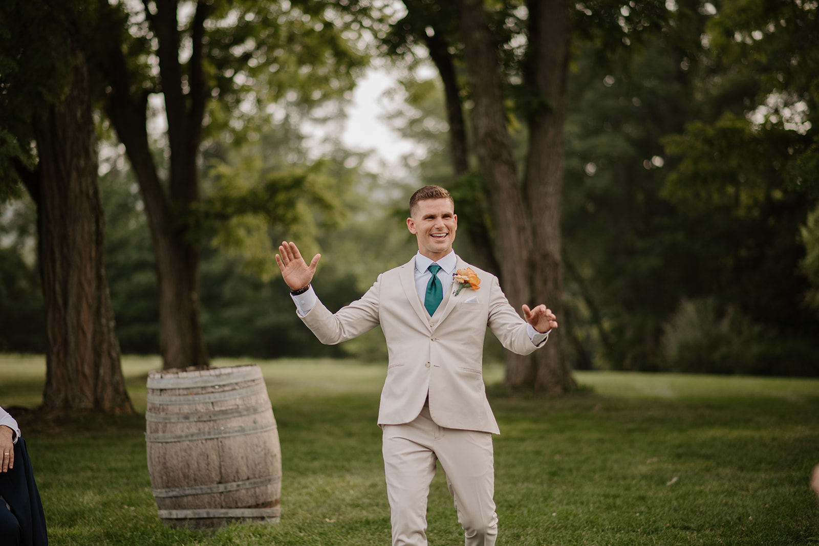 Groom raises his arms in celebration on the lawn beside a wine barrel.