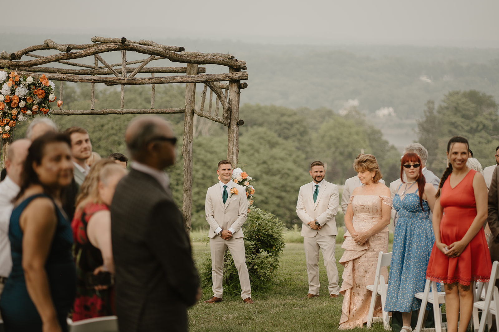Guests stand for the ceremony beneath the wooden arch overlooking the valley.