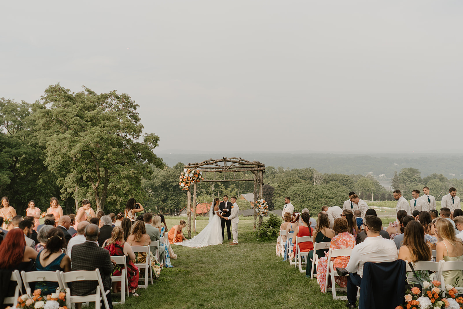 Wide view of the hilltop ceremony with guests seated on either side of the aisle.