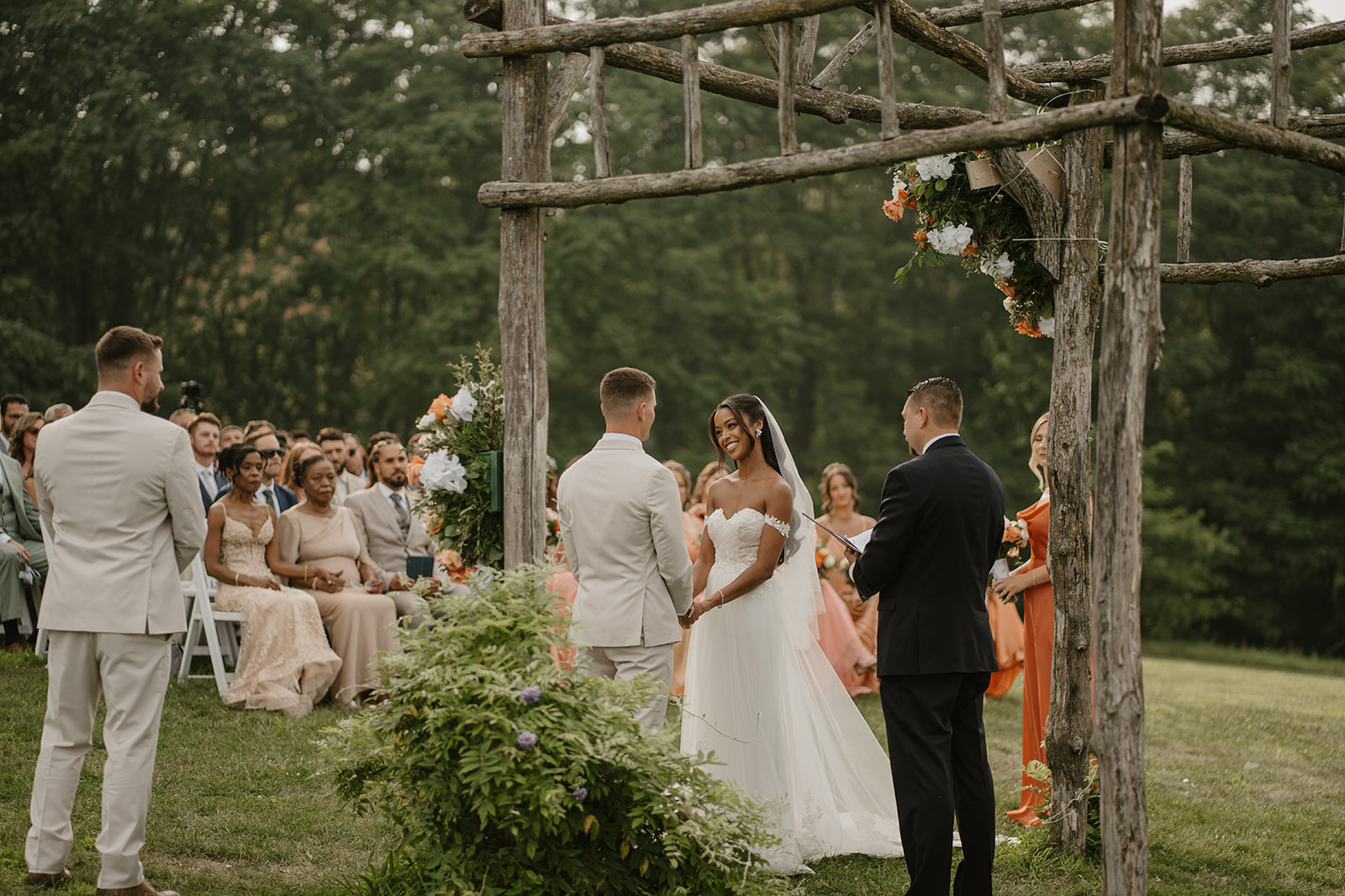 Bride and groom face each other at the floral arch during their vows.