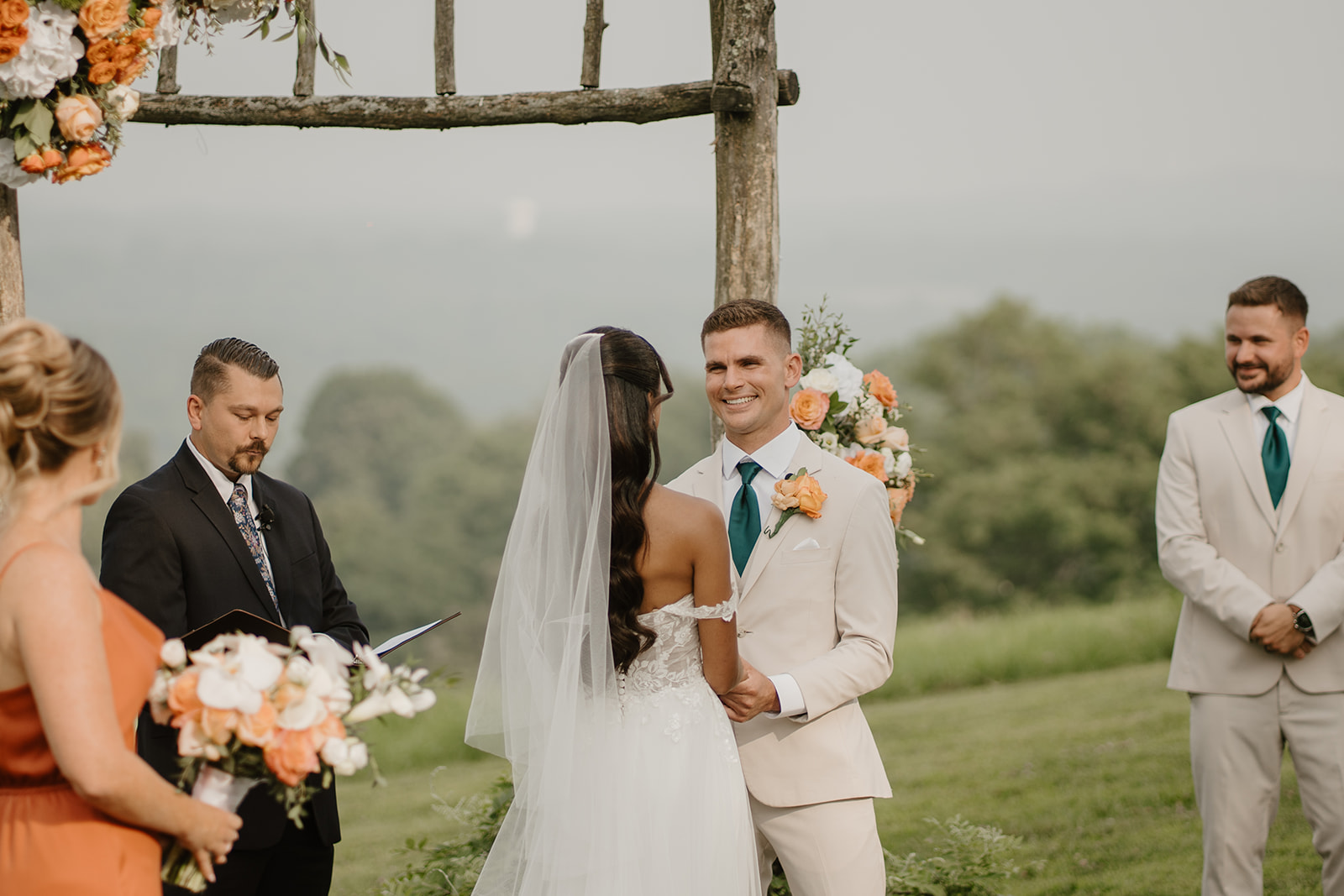 Bride and groom smile at each other during their ceremony, veil catching the breeze.