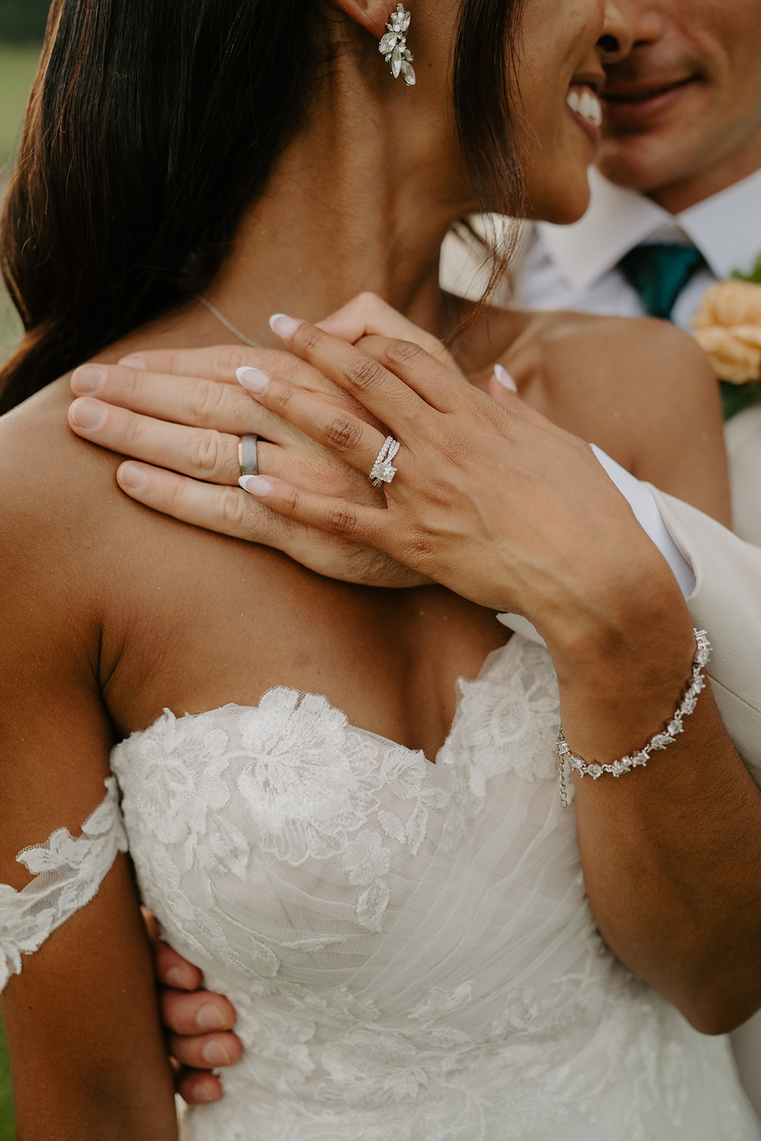 Close-up of the bride's hands and wedding rings resting on the groom's shoulder.