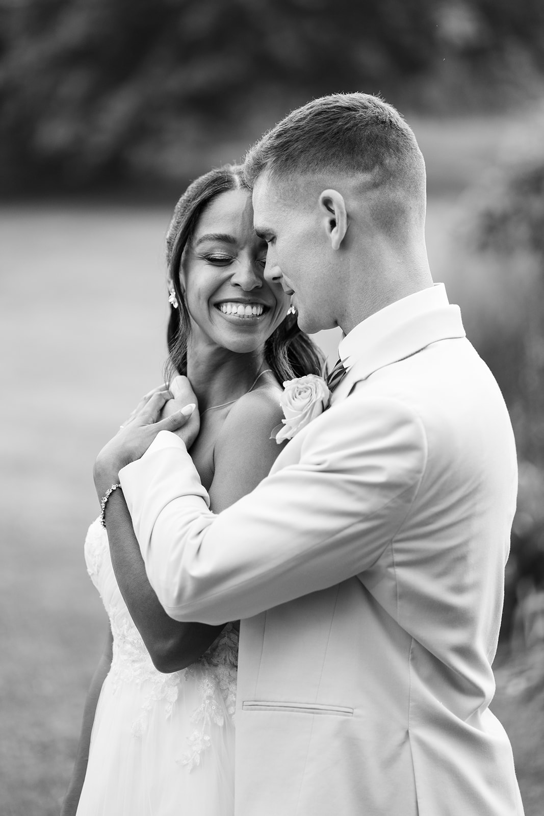 Black and white portrait of the bride smiling as the groom holds her close.