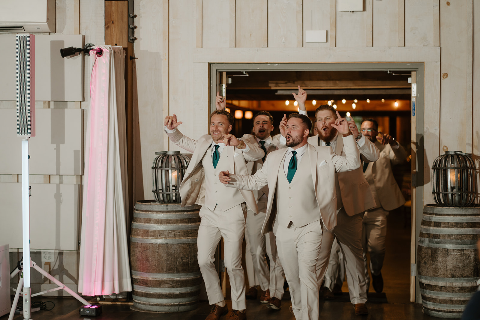 Groomsmen burst into the reception past the wine barrels, arms in the air.