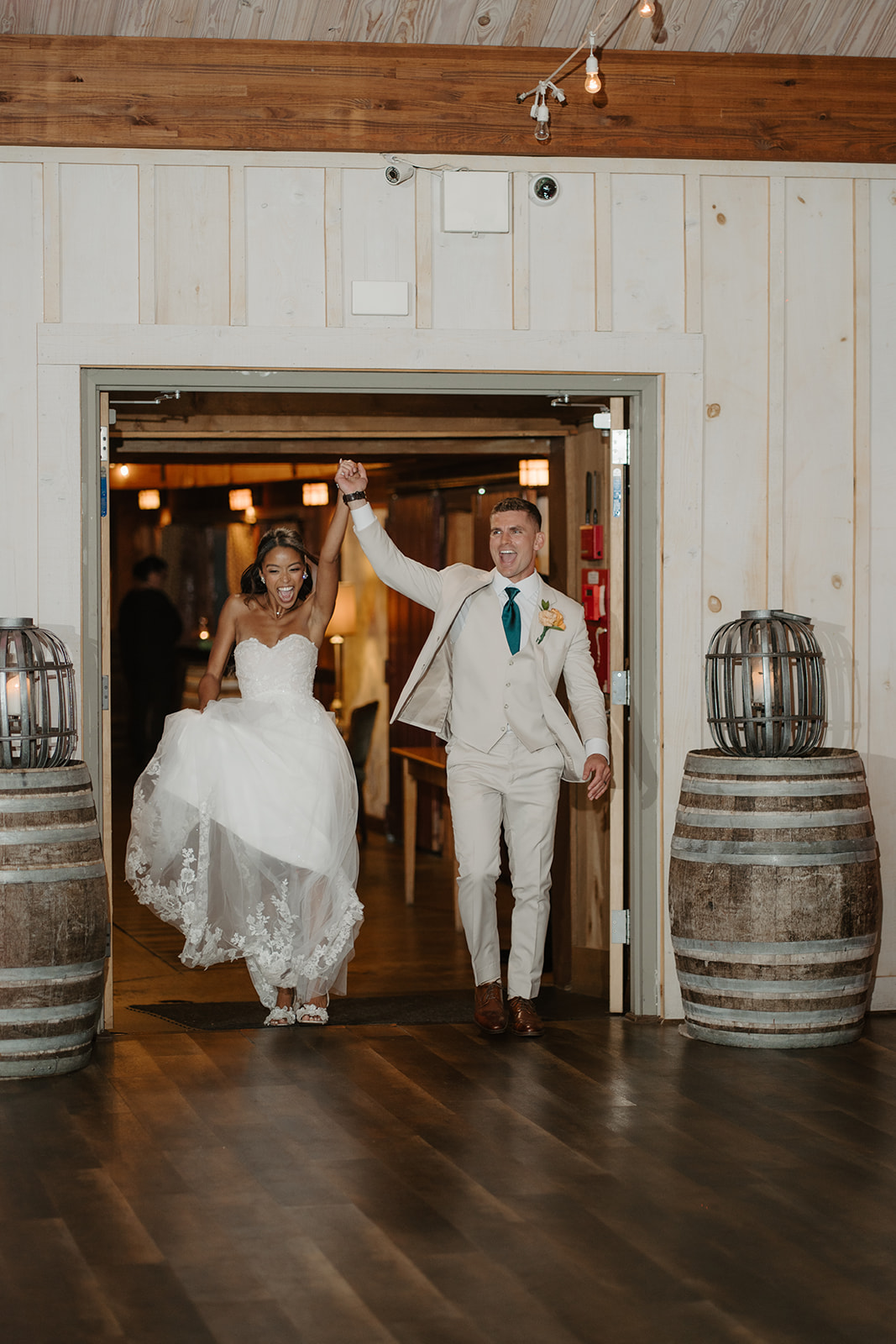 Groom lifts the bride's hand as they enter the barn reception together.