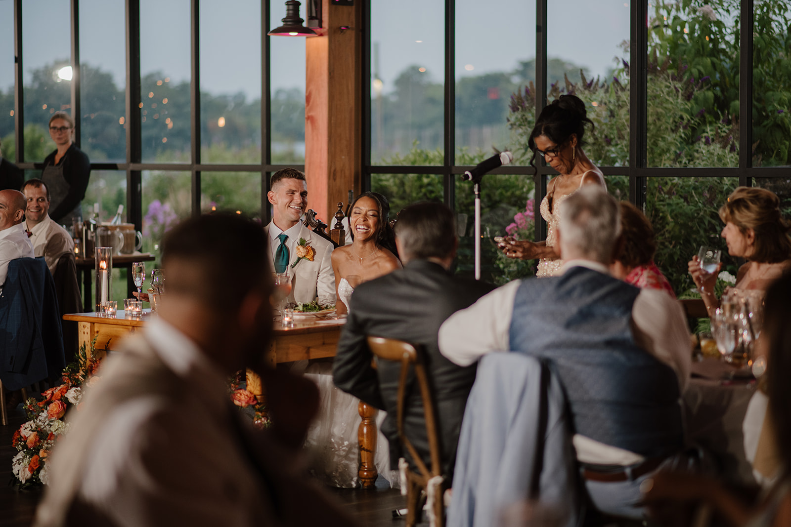 Guests listen to speeches at the candlelit tables beside the barn windows.