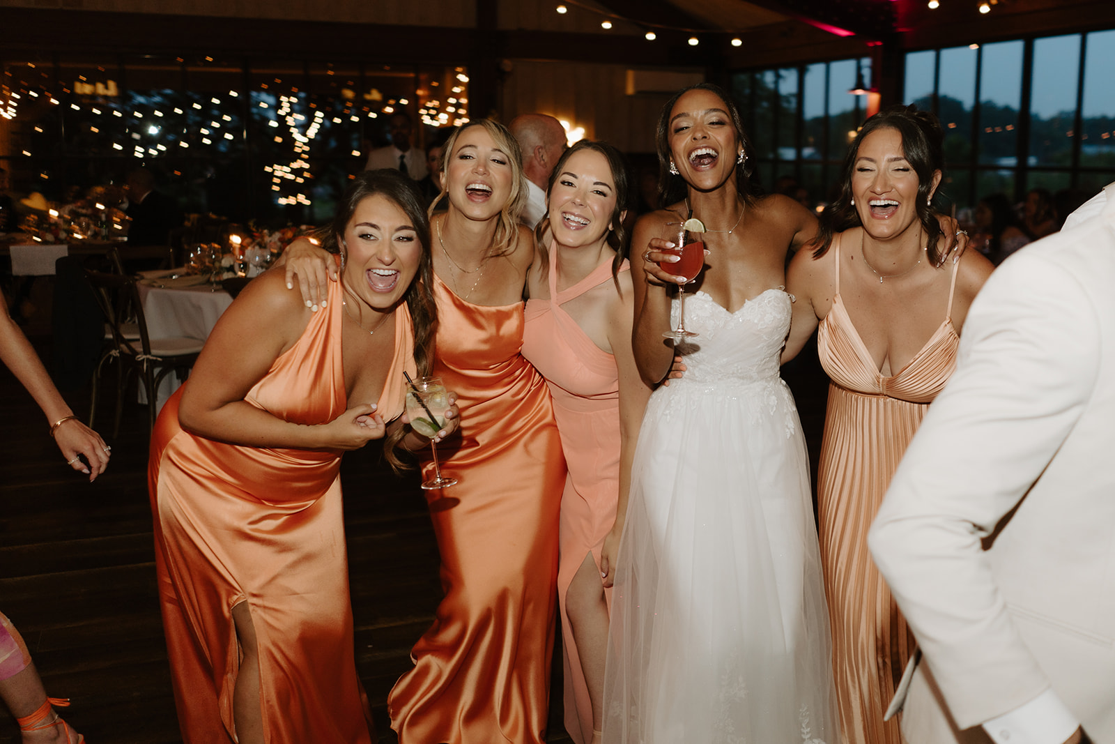 Bride laughs with her bridesmaids in coral gowns during the reception party.